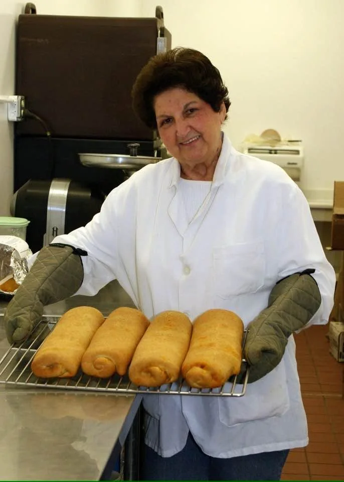A woman in a white shop coat holding a tray of freshly baked sausage rolls